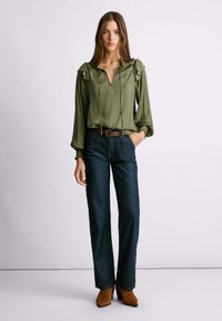 Blusa verde oliva con dettagli arricciati, abbinata a jeans a gamba larga blu scuro e stivali con tacco marroni. Design semplice con vestibilità comoda.