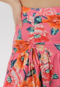 Blumiger Rock aus pinkem Stoff mit großen orangen und weißen Blumen. Design mit gerafftem Bund und Kordelzug. Weicher Stoff.
