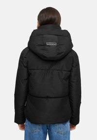 Black puffer jacket with a hood, quilted design, and a logo on the back. Features long sleeves and a slim fit at the waist.
