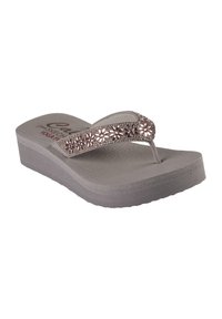 Grijze flip-flop sandaal met een gestructureerde voetbed en een wigzool. De band heeft bloemmotieven met metalen accenten.