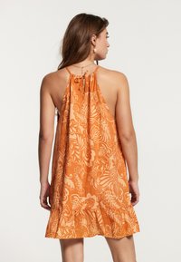 Vestido halter naranja con flores y dobladillo con volantes, hecho de tejido ligero, que presenta un cierre de lazo en la parte posterior y una silueta fluida.