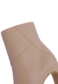 Botín beige hasta el tobillo hecho de cuero suave, con un diseño ajustado, detalles de costura sutiles y una punta redondeada con un corte abierto.