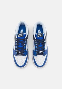 A Nike sportcipő fehér bőr alapja kék bőr részletekkel, tengerészkék fűzőkkel, perforált orr résszel és Nike logóval rendelkezik a nyelvén.