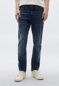 Tamnoplave traperice ravnih nogavica s klasičnim stilom s pet džepova i suptilnim izblijedjenjem. Uparen s tenisicama svijetle boje.