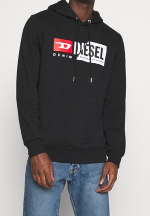 Czarna bluza Diesel z kapturem, z przednią kieszenią typu kangurka oraz białym i czerwonym logo, noszona z niebieskimi dżinsami, pokazująca górną część ciała i ręce.