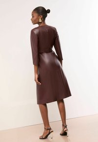 Rochie din piele bordeaux cu mâneci trei sferturi și corset ajustat, având o textură netedă și o fustă până la genunchi.