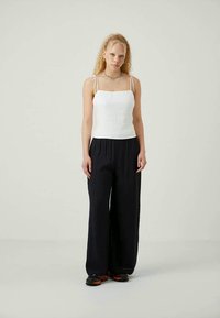 Top de linho branco com alças finas, combinado com calças largas azuis-marinho. O modelo está de pé sobre um fundo claro, sem detalhes adicionais.