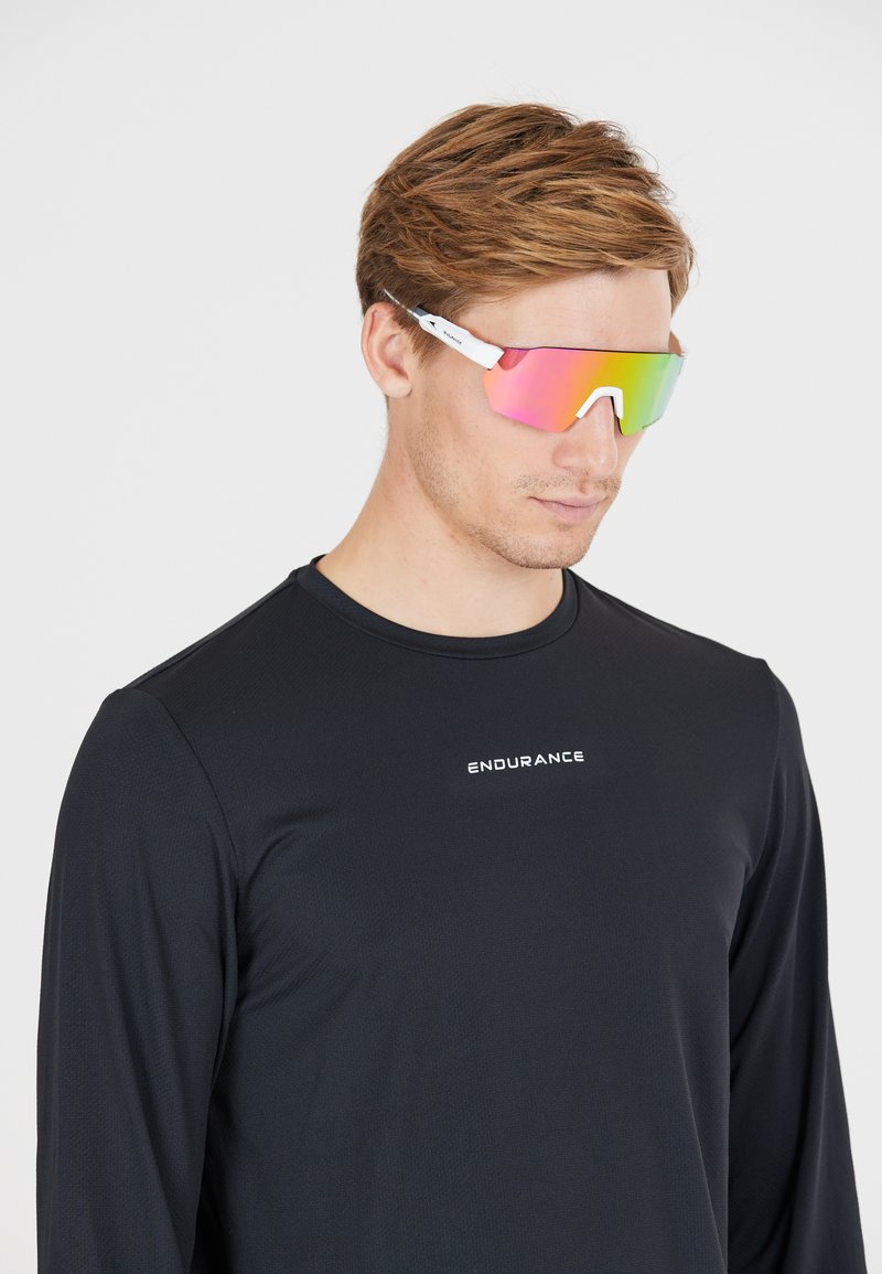 Zonnebril met een reflecterende roze lens en een wit montuur. Draagt door een persoon in een zwart longsleeve shirt, wat een slank, sportief design benadrukt.