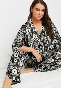 Svart och vit mönstrad satinpajamaset med blommönster, avslappnad passform och skört krage. Byxorna har vida ben och knappstängning.