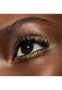 Nahaufnahme eines Auges mit dunklen Wimpern, goldfarbenem Augen-Make-up mit schimmernden Akzenten und einem glatten, tiefbraunen Hautton, der das Auge umgibt.