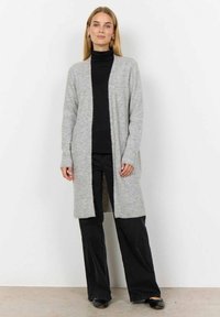 Lichtgrijze gebreide cardigan met open voorkant, lange mouwen, geribbelde textuur en zijzakken, gecombineerd met een zwarte top en zwarte broek.