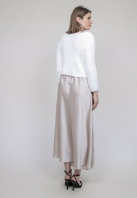 Un pull court texturé blanc associé à une jupe maxi en satin beige. Des sandales à talons noirs avec des lanières complètent l'ensemble. Visible de dos.