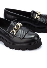 Mocasines de cuero negro con un acento de cadena dorada, detalle de flecos texturizados en la parte del mar y una suela gruesa de goma negra.