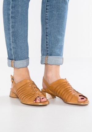 Tan læder slingback sandaler med horisontale folder og åben tå. Har en lav træhæl og justerbar rem. Sammen med rullede jeans.