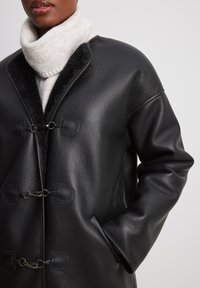 Cappotto in pelle nera con finitura testurizzata, caratterizzato da un colletto alto, chiusure a scorrimento e tasche laterali con un interno in misto lana.