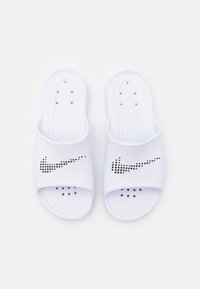 White slide sandals made of smooth synthetic material, featuring a large black dot-patterned Nike logo on the strap and textured footbed.