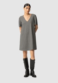 Sukienka na krótki rękaw w serek w czarno-białą kratkę, wykonana z materiału o luźnym, swobodnym kroju, zestawiona z czarnymi kozaczkami do kolan.