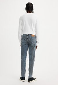 Lätt vit långärmad skjorta, kombinerad med blekta blå jeans och svarta sneakers. Jeans har en läderpatch på baksidan.