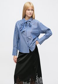 Blauw-wit gestreepte blouse met een strik bij de kraag, gecombineerd met een zwarte satijnen rok met een kanten zoomdetail.