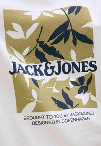 Hvid t-shirt med et guld- og marineblåt grafisk design med blade. Inkluderer teksten "JACK & JONES" og "DESIGNED IN COPENHAGEN."