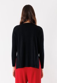 Maglione nero a maglia con maniche lunghe e scollatura rotonda. Il tessuto appare morbido e liscio, con una vestibilità leggermente ampia all'orlo.