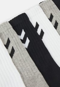 Négy pár zokni fekete, fehér, szürke és világosszürke színben, bordázott textúrával és kontrasztos színű zigzag mintával.