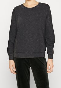 Sudadera gris oscuro hecha de una tela suave, con un escote redondeado, mangas largas y un corte holgado con un dobladillo ligeramente recortado.