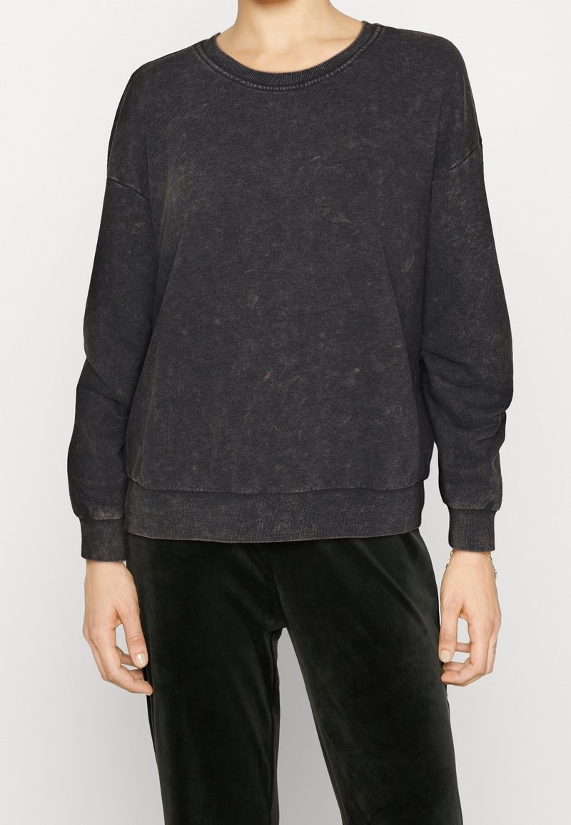 Sudadera gris oscuro hecha de una tela suave, con un escote redondeado, mangas largas y un corte holgado con un dobladillo ligeramente recortado.