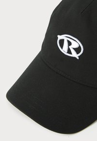 Svart bomullslue med buet skygge, med en brodert hvit logo på forsiden. Teksturen er jevn med et lett strukturert design.