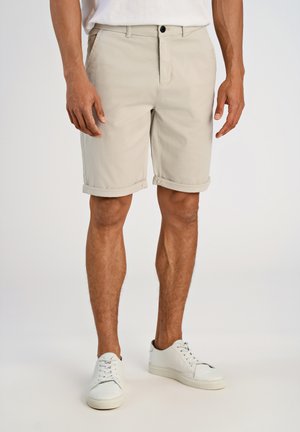 Beige katoenen shorts met opgerolde zoom, voorzakken en een enkele knoopsluiting, gecombineerd met witte sneakers op een neutrale achtergrond.
