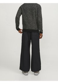Maglione grigio scuro lavorato a maglia con finitura testurizzata, abbinato a pantaloni neri larghi e sneakers grigie. Mette in risalto il comfort e lo stile casual.