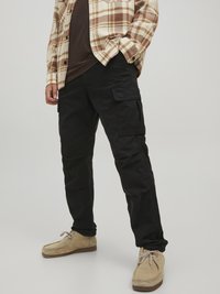 Schwarze Cargo-Hosen aus strapazierfähigem Stoff, mit mehreren Taschen, einem schmalen Schnitt und einer glatten Textur, kombiniert mit beigen Wildlederschuhen.