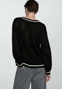 Pull noir en maille avec une coupe ample, présentant un ourlet et des poignets à rayures blanches. Le design comprend un tissage ouvert et des épaules tombantes.