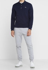 Námořnická polokošile s dlouhým rukávem, límečkem a třemi knoflíky, spárovaná se světle šedými joggingovými kalhotami a bílými teniskami.