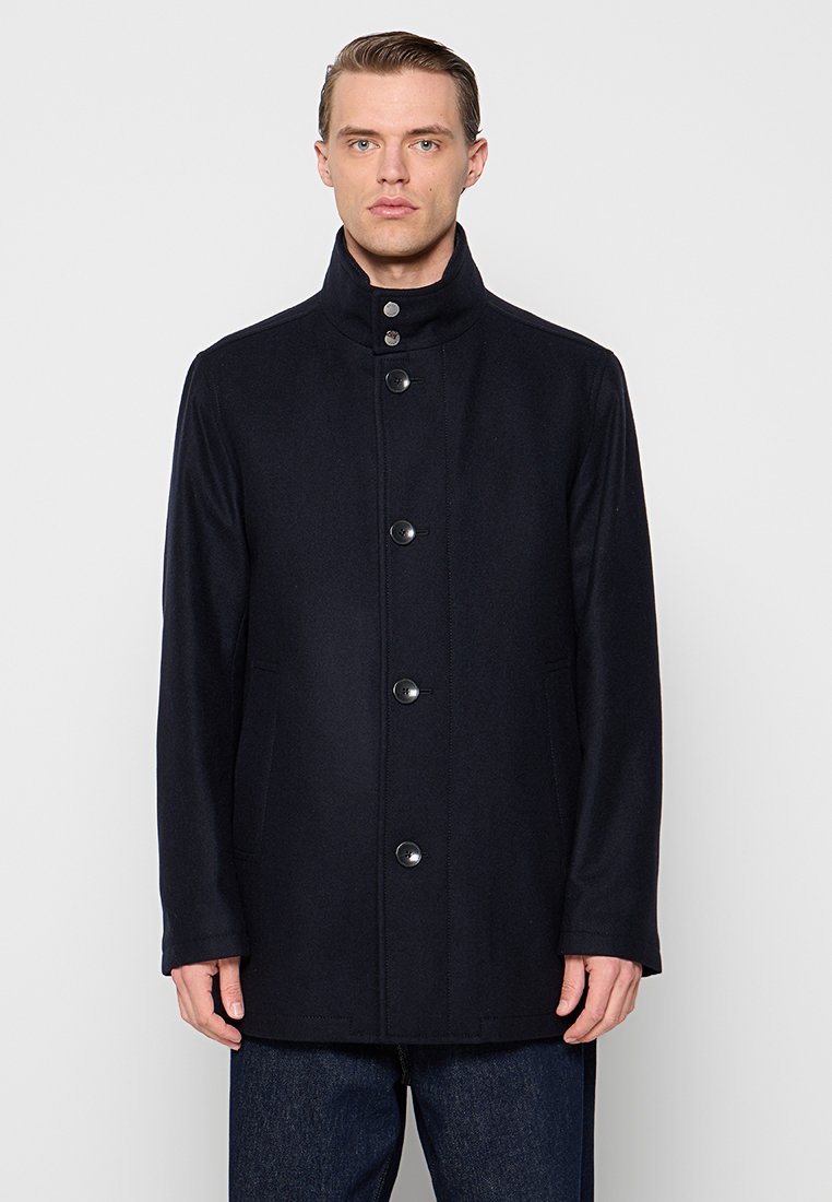 Cappotto in misto lana di colore blu navy con colletto alto, dotato di chiusura frontale con bottoni e due tasche laterali, che offre una silhouette strutturata.