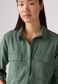 Groen overhemddas gemaakt van zacht materiaal, met twee borstzakken, een klassieke kraag en een klein rood Levi's logo label aan de zijkant.