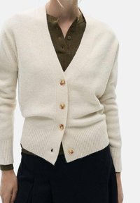 Cardigan couleur crème en tissu doux, avec un col en V profond, des poignets côtelés, trois boutons en bois et une finition légèrement texturée.