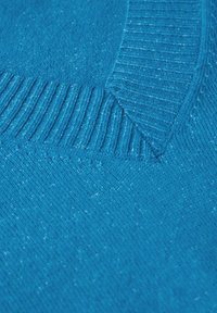 Turkusowy sweter z prążkowanym dekoltem i gładką fakturą. Ma czysty design i subtelne drobinki w całym materiale.