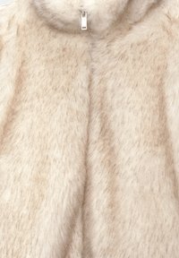 Tissu en fausse fourrure beige clair avec une texture douce, doté d'un col haut et d'une fermeture éclair argentée au niveau du cou.