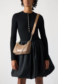 Zwarte geribbelde jurk met lange mouwen en een knoopsluiting bij de hals. Bruine geembosste handtas met kettingdetails en merkstrap.