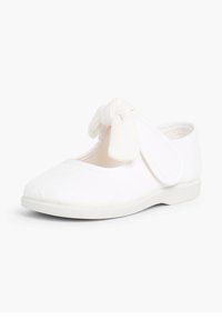 Weiße Stoffschuhe mit strukturiertem Finish, abgerundeter Zehe, Klettverschlussriemen und einem Knotenakzent an der Seite. Flache weiße Sohle.