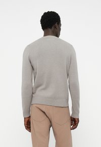 Grauer Strickpullover mit gerippten Kanten und Rundhalsausschnitt, kombiniert mit beigen Hosen. Das Design zeichnet sich durch eine glatte Textur und eine klassische Passform aus.