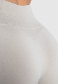 Lichtgrijze fitted stof met een gladde, elastische textuur. Hoog halsontwerp met ribbelstructuur langs de naden.