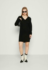 Vestido preto de manga longa com decote em V, feito de um material suave. Combinado com botas de tornozelo com padrão de vaca e uma pequena bolsa preta.