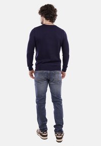 Maglione a maglia blu navy con maniche lunghe e colletto rotondo, abbinato a jeans in denim blu e scarpe sportive con dettagli bianchi.