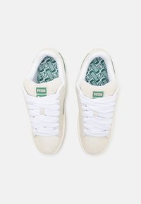 Baskets en cuir suédé blanc avec logo vert, lacets blancs plats et semelles intérieures vertes à motifs. Bout rond et tige légèrement texturée.