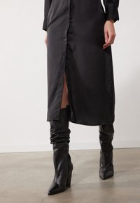 Sort satin skjortekjole med knap-front, sideslids, parret med knæhøje sorte læder spidse støvler med en samlet tekstur.