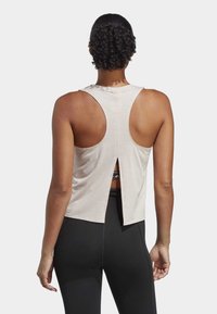 Top senza maniche beige chiaro con scollatura rotonda, design con schiena scoperta e dettaglio svasato nell'orlo. Abbinato a leggings neri.
