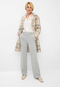 Tjekket uldfrakke i beige og grå, hvid skjorte med knapper, grå pinstribede bukser og beige loafers. Lommer synlige i bukserne.