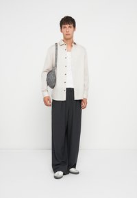 Light beige button-up shirt, gray crossbody bag, dark wide-leg trousers, and gray-and-white sneakers. Minimalistic design and soft textures.